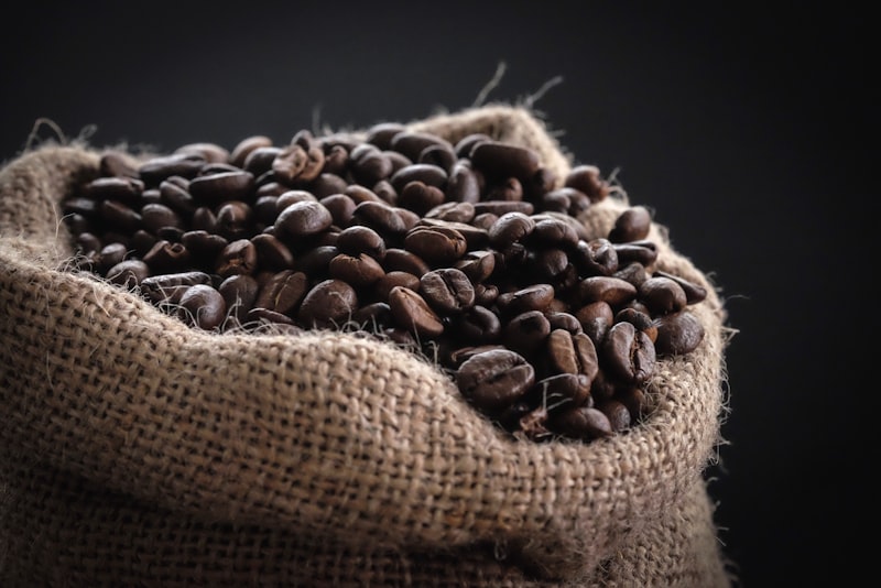 A hand holding a scoop of whole roasted coffee beans.