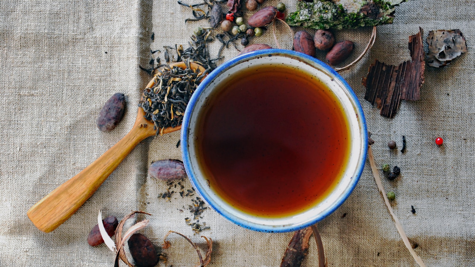 Whole loose-leaf tea leaves in a wooden scoop beside a cup.
