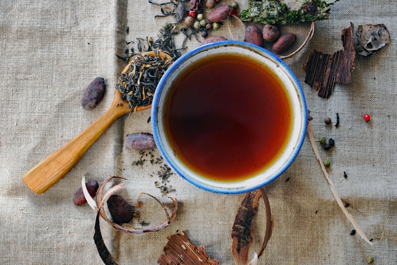 Whole loose-leaf tea leaves in a wooden scoop beside a cup.