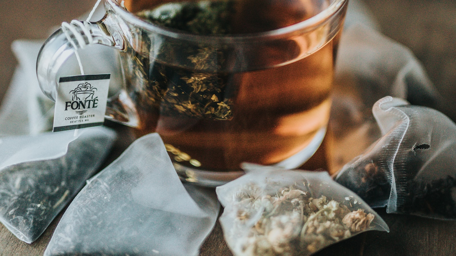 A ceramic teapot and a loose-leaf infuser on a wooden tray beside a cup of tea.
